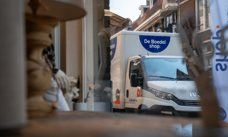 Wit busje van De Boedel Shop als gezien door een raam